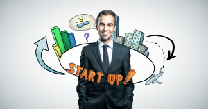 Businessman in a suit standing in front of startup-themed illustrations including buildings, graphs, and the word "START UP!"