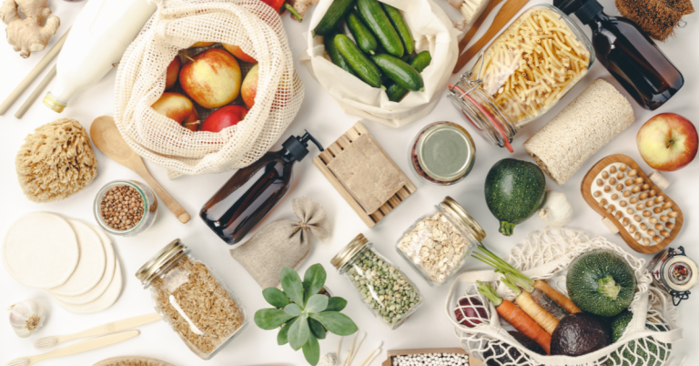 A variety of eco-friendly products including reusable bags, glass jars, and fresh produce laid out on a white surface.