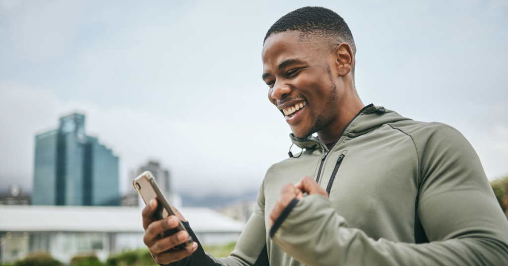 Man smiling while looking at his smartphone during an outdoor workout.