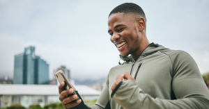 Man smiling while looking at his smartphone during an outdoor workout.