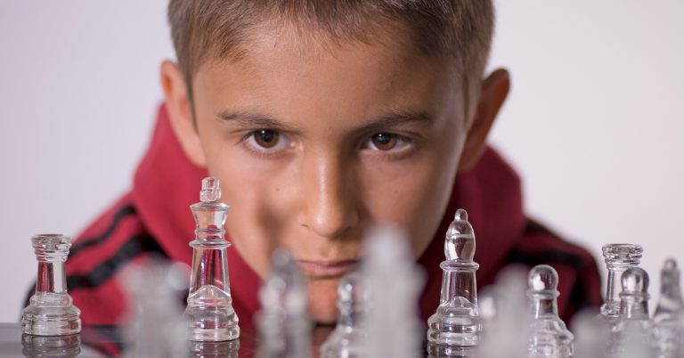 A young boy intensely focused on a chessboard with glass chess pieces.