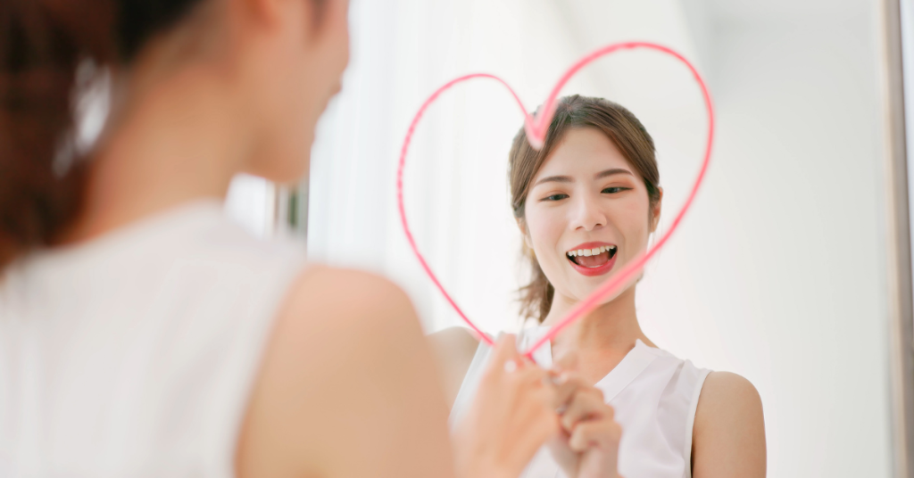 Woman drawing a heart on a mirror, smiling and focusing on self-care.