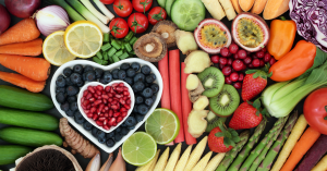 A variety of colorful fruits and vegetables arranged around a heart-shaped bowl filled with berries.